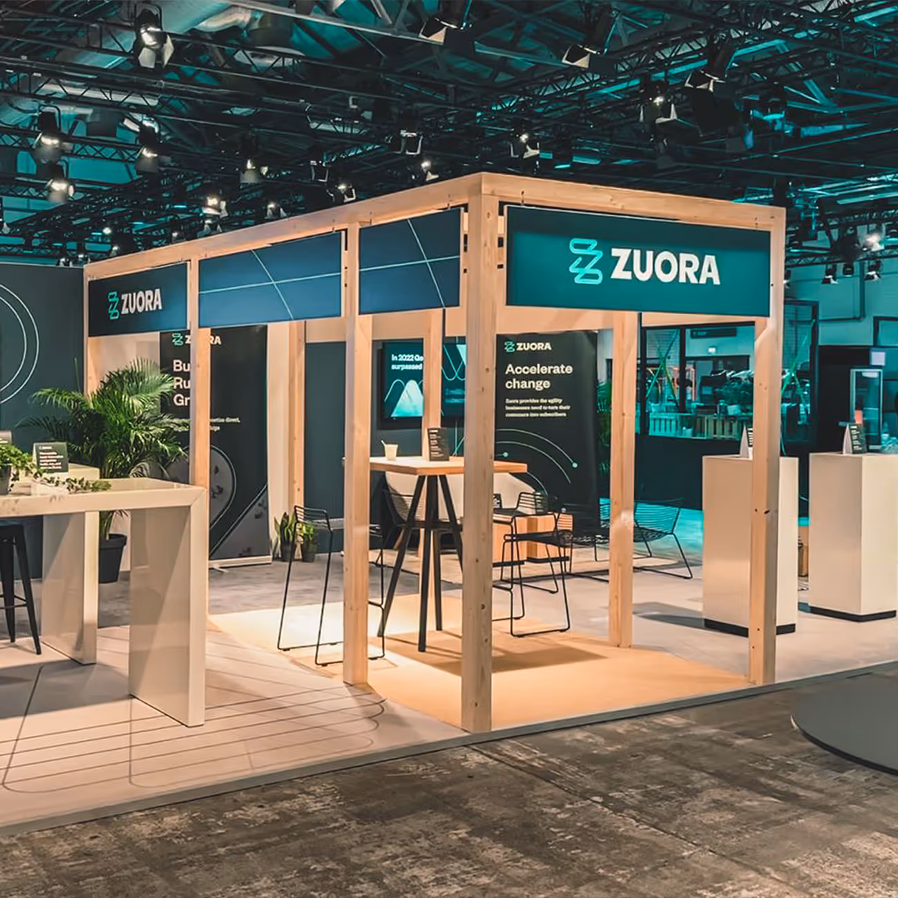 Modern trade show booth with wooden frame and Zuora branding, featuring tall tables, chairs, and informational banners.