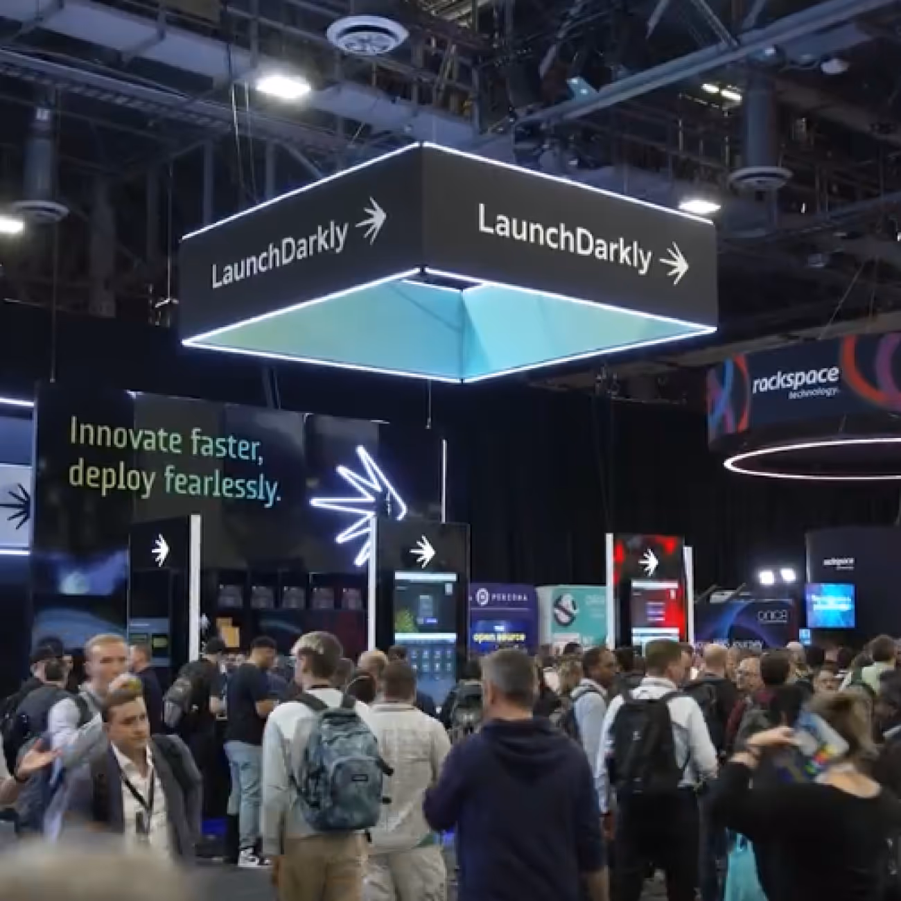 Crowded tech trade show with a large hanging LaunchDarkly sign and a booth displaying 'Innovate faster, deploy fearlessly.'