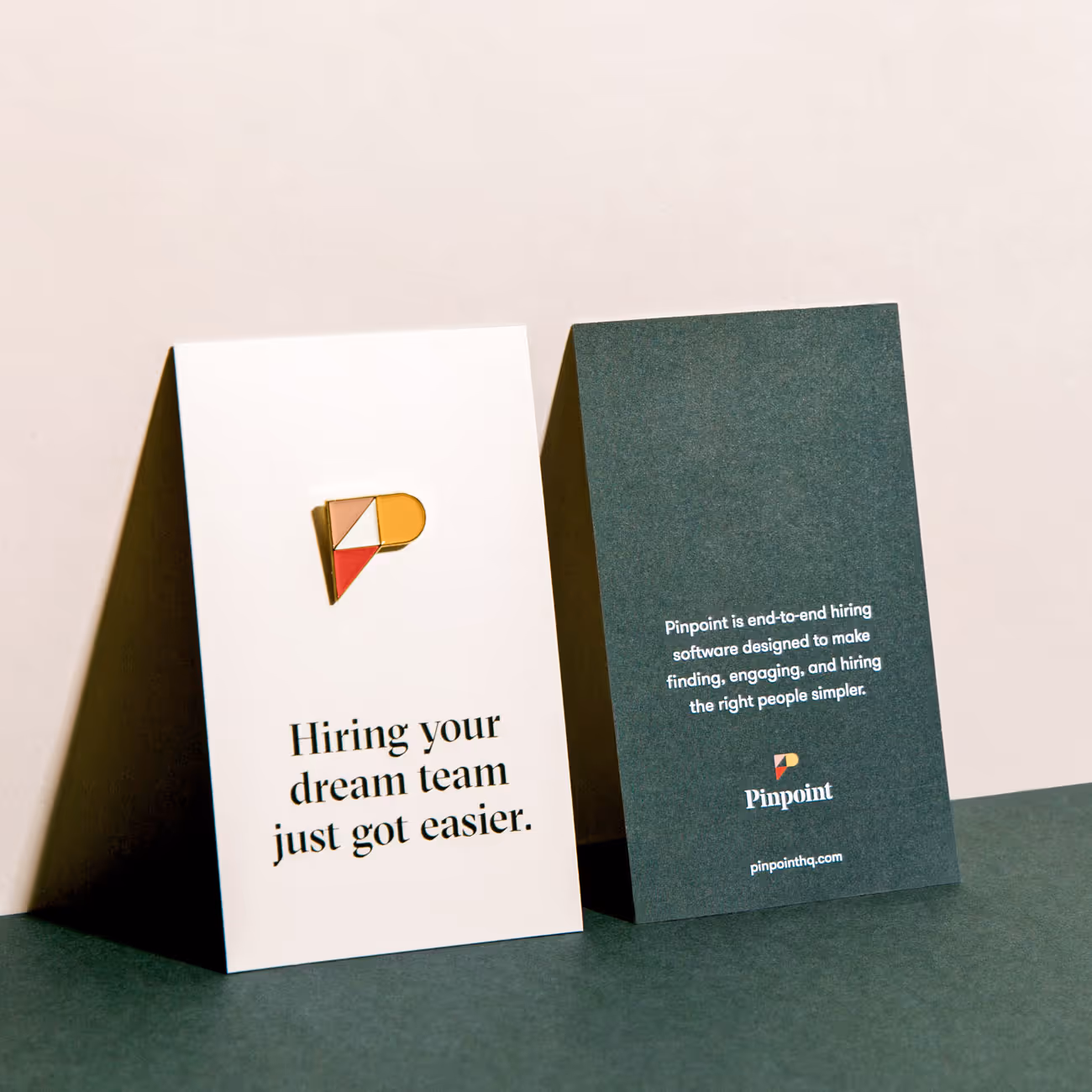 Two standing cards, one white with a colorful 'P' pin and text 'Hiring your dream team just got easier.' The other dark green with white text about Pinpoint hiring software and its website.