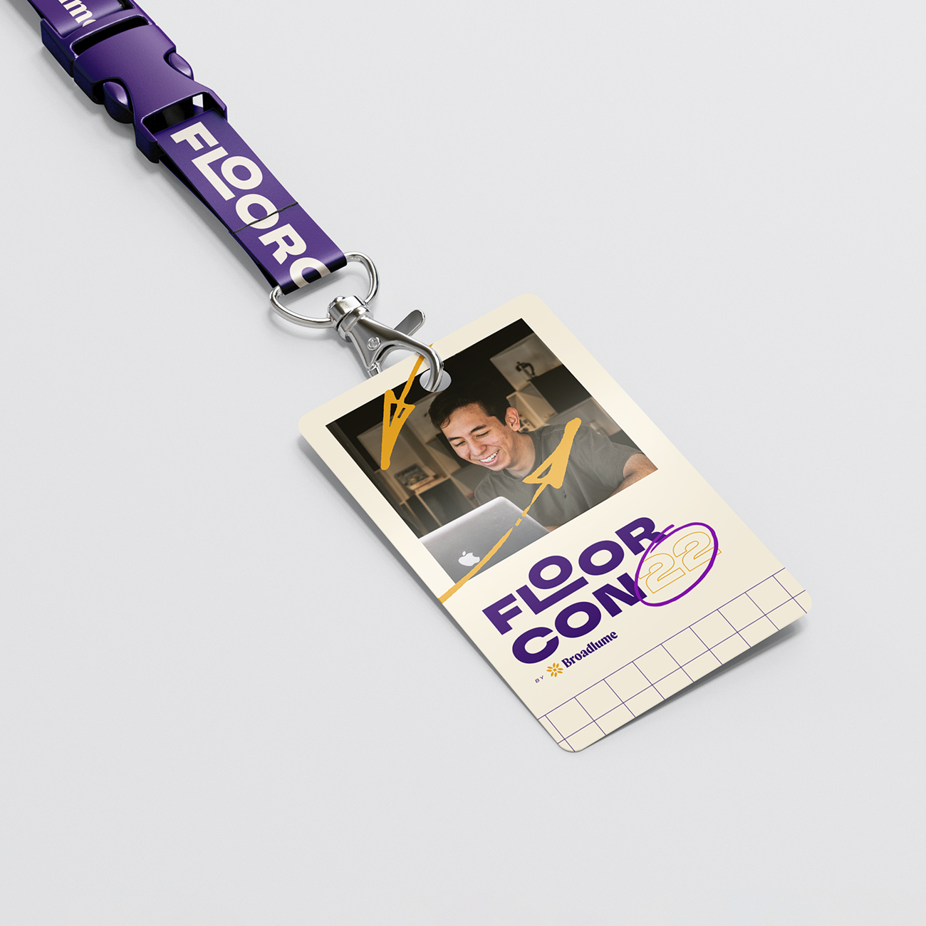 Event badge with a smiling man using a laptop and text 'FLOOR CON 22 by Broadlume' on a purple lanyard.